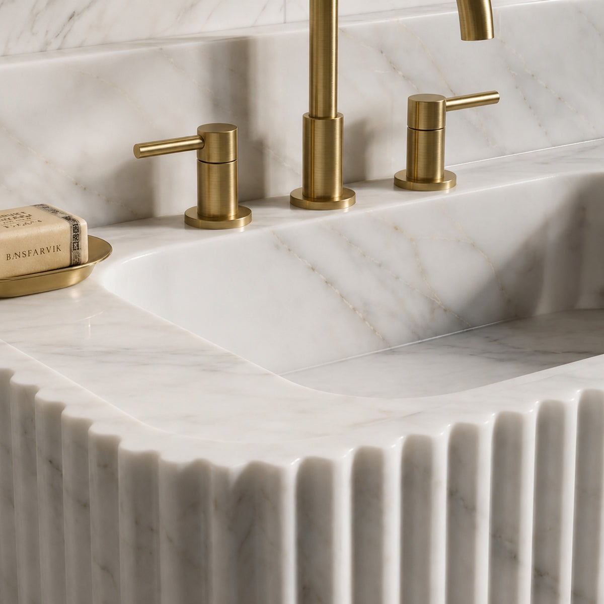 Carrara White marble sink styled with green leafy branches in a dark glass vase on the left side of the basin