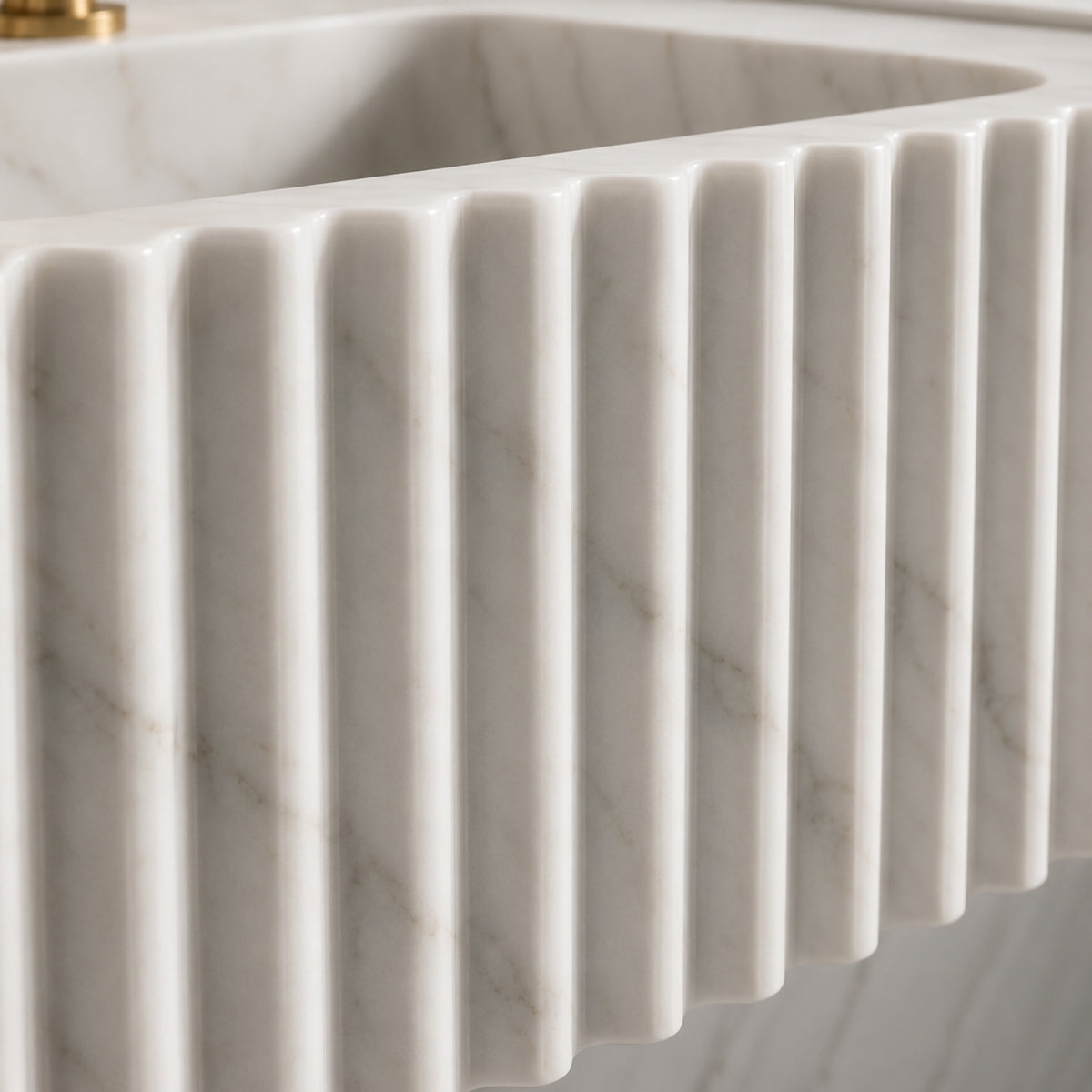 Carrara marble sink with a black soap dispenser placed on the right side, green branches on the left, and gold wall-mounted tapware.