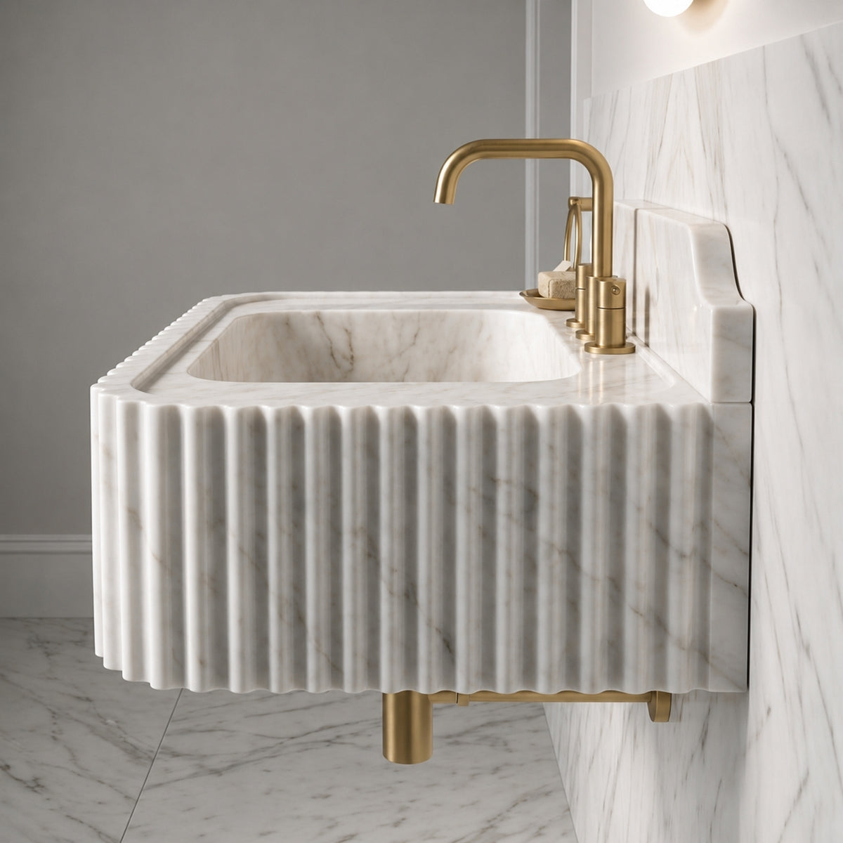 Marble bathroom sink with a fluted Carrara White exterior, pale grey veining, and a matching stone backsplash behind the faucet.