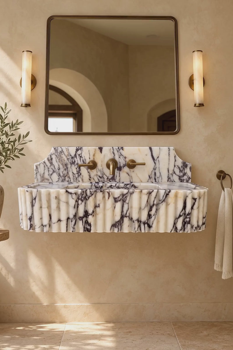 Handcrafted Calacatta Viola marble floating bathroom sink featuring sculpted vertical fluting, integrated rectangular basin and elegant brass fixtures.